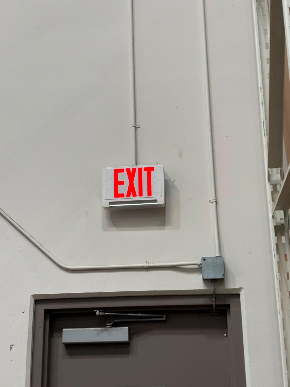LED exit sign wired in surface conduit above a warehouse door
